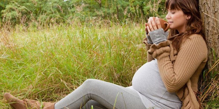 Беременная женщина пьет чай на природе