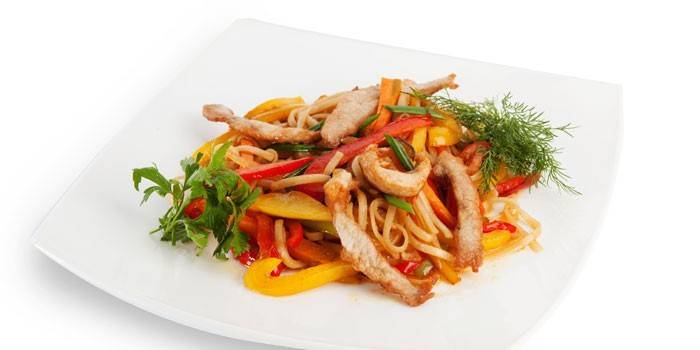 Удон с овощами и кусочками свиного мяса на тарелке