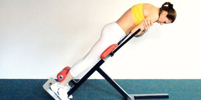 Девушка на тренажере выполняет гиперэкстензию с круглой спиной 