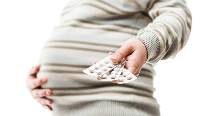 Беременная женщина показывает блестеры с таблетками