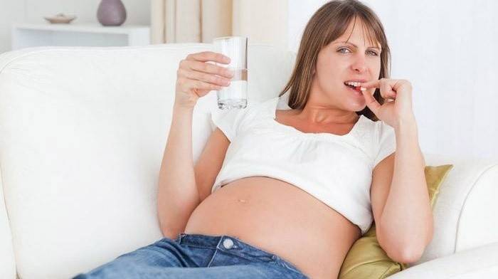 Беременная женщина пьет витамины с кальцием