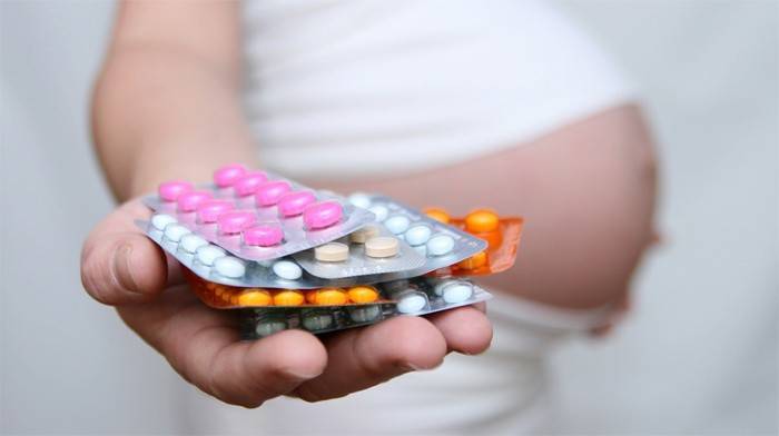 Беременная женщина держит на ладони таблетки