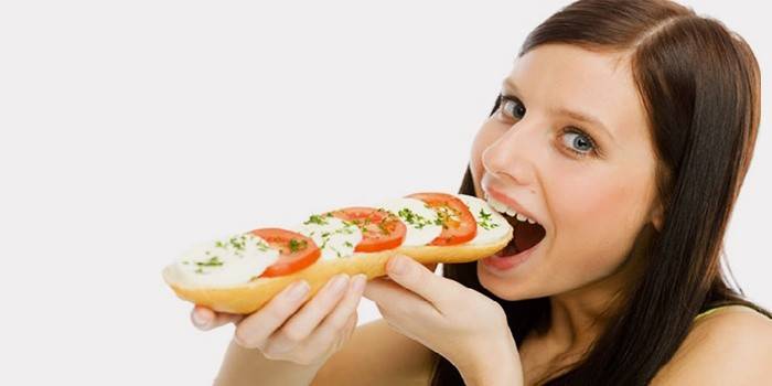 Девушка кушает бутерброд с помидорами и сыром