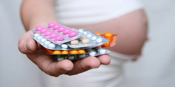 Беременная девушка держит в руке гормональные таблетки