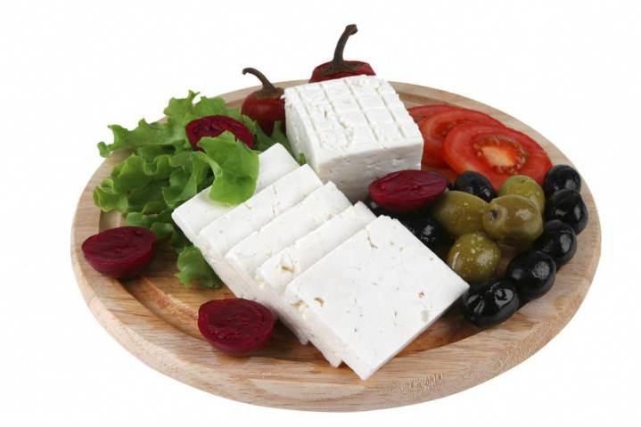 На тарелке сыр, оливки, листья салата