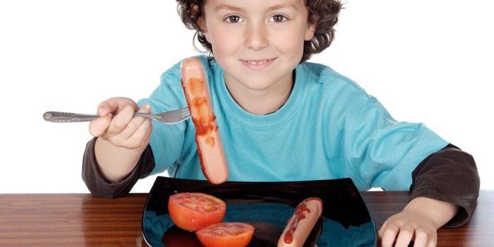 Мальчик ест сосиски