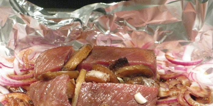 Куски мяса с луком и картофелем в фольге перед запеканием