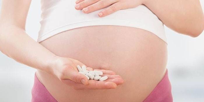 Беременная женщина держит на ладоне таблетки