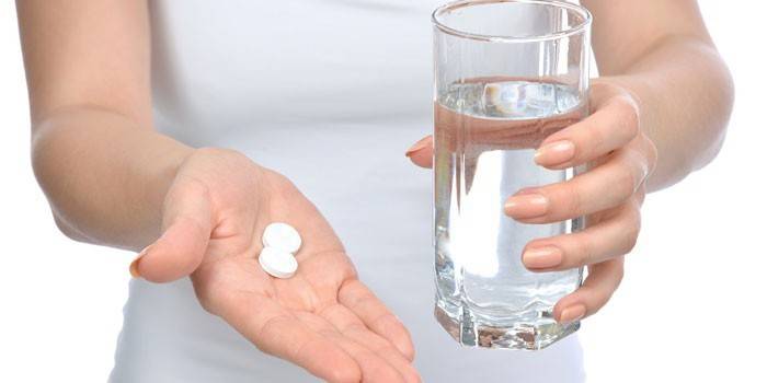 Таблетки на ладони и стакан воды