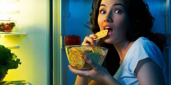 Девушка ест крекер перед открытым холодильником