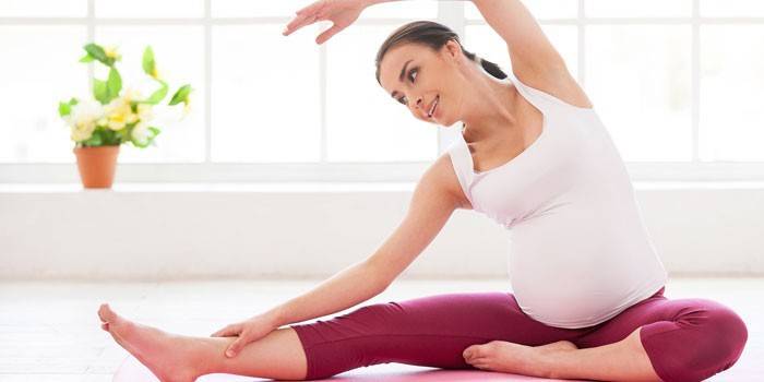 Беременная женщина выполняет упражнение сидя на полу