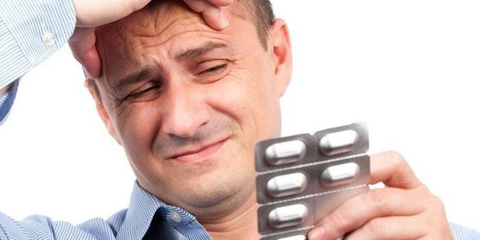 Мужчина с головной болью держит в руке блистер с таблетками
