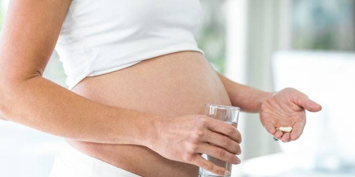 Беременная женщина со стаканом воды и таблетками 