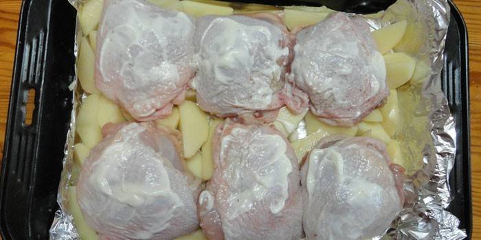 Куриные бедрышки на подушке из картофелем перед выпеканием на противне