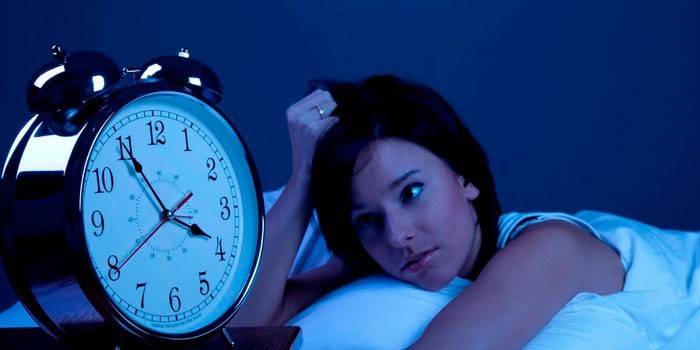 Девушка лежит в кровати и смотрит на будильник