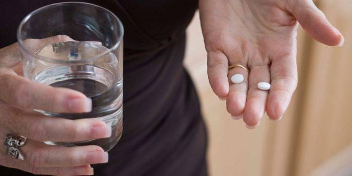 Женщина держит таблетки и стакан воды в руках