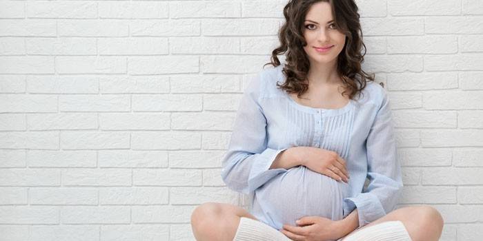 Беременная девушка сидит у стены