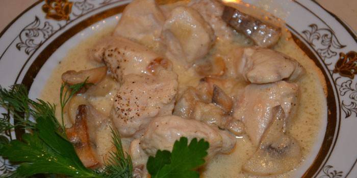 Кусочки куриного мяса с шампиньонами в сметанном соусе на тарелке