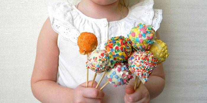 Девочка держит в руках кейк-попсы с разноцветной посыпкой 