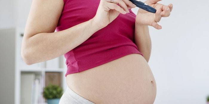 Беременная девушка проверяет уровень сахара в крови с помощью глюкометра