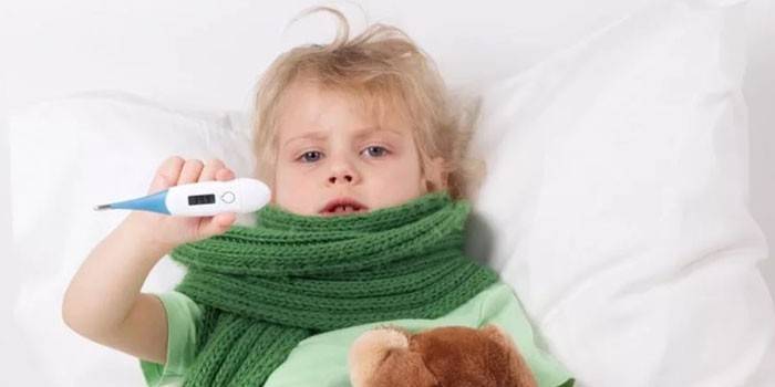 Ребенок лежит в постели и держит электронный градусник в руке
