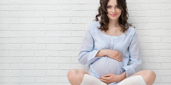 Беременная девушка сидит у стены
