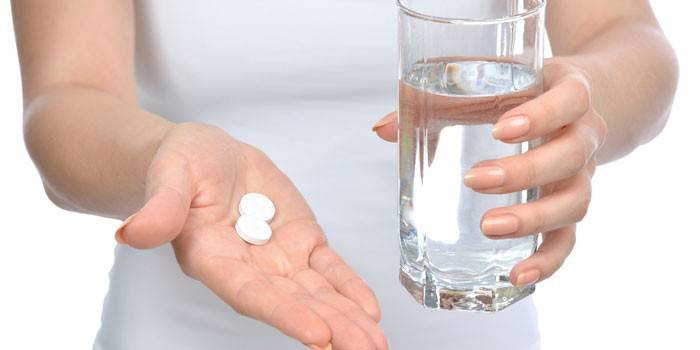 Таблетки и стакан воды в руках у девушки