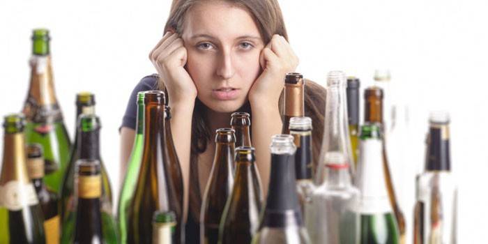 Девушка сидит за столом с пустыми бутылками из-под спиртного