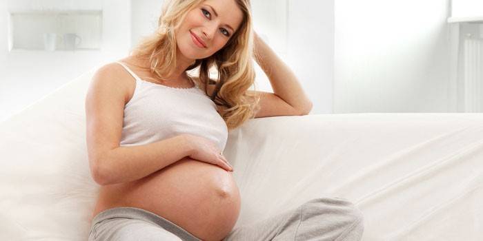 Беременная девушка сидит на диване 