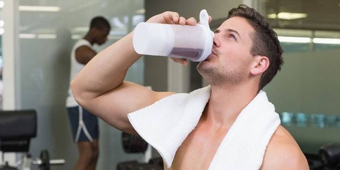 Мужчина в спортзале пьет протеиновый коктейль