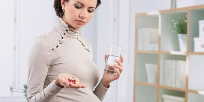 Беременная девушка с таблетками и стаканом воды