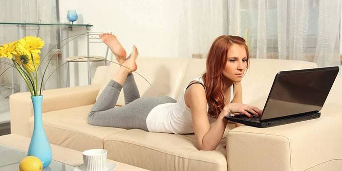 Девушка лежит на диване с ноутбуком