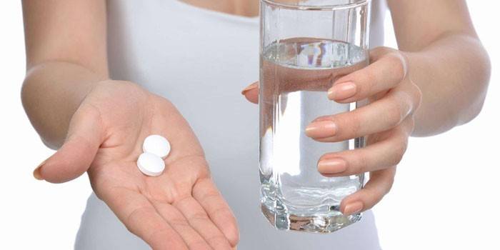 Таблетки и стакан воды в руках у девушки