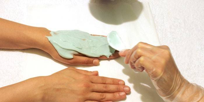 Девушке делают маску из глины для рук