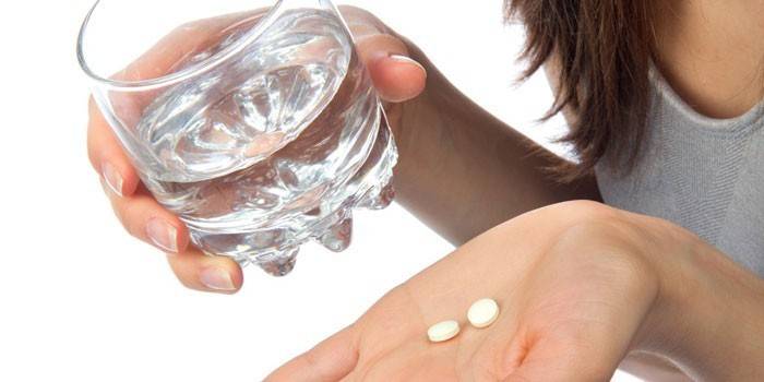 Девушка держит таблетки на ладони и стакан воды в руке