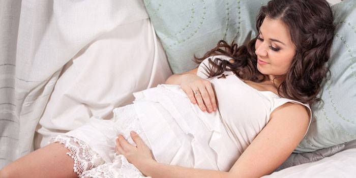 Беременная девушка лежит на подушках