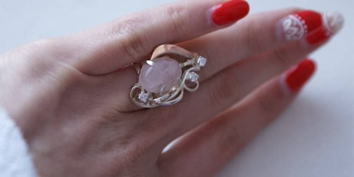Золотое кольцо с розовым кварцем на руке женщины