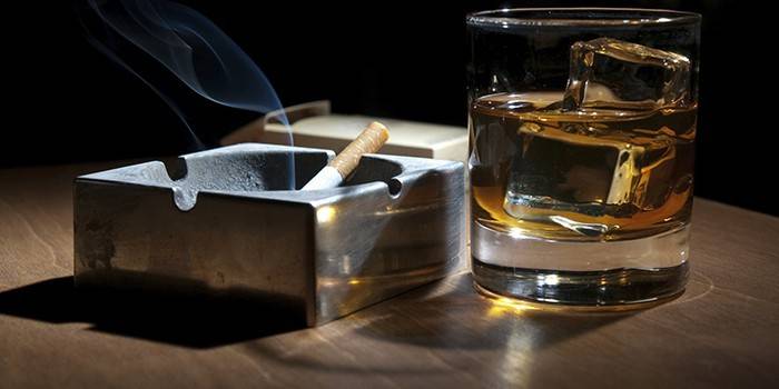 Сигарета в пепельнице и стакан с алкоголем и льдом
