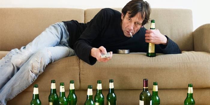 Мужчина на диване с сигаретой в окружении пустых бутылок