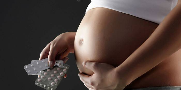 Беременная женщина держит в руке таблетки