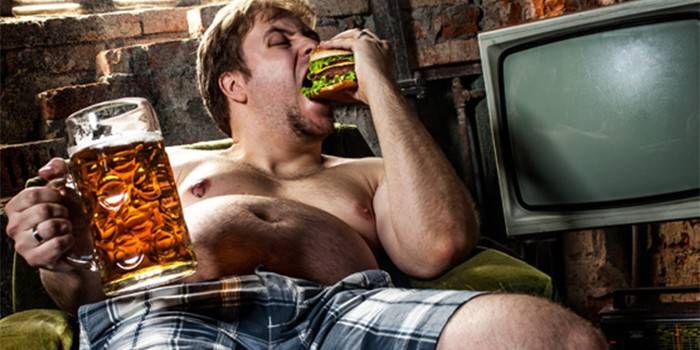 Мужчина ест гамбургер и держит бокал пива