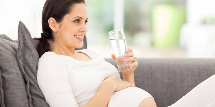 Беременная женщина держит стакан воды