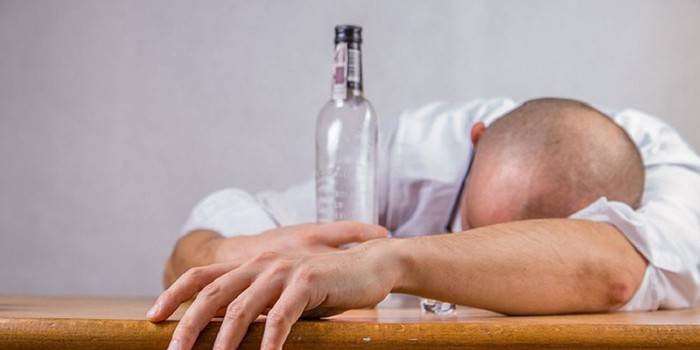 Пьяный мужчина лежит на столе и держит пустую бутылку в руке