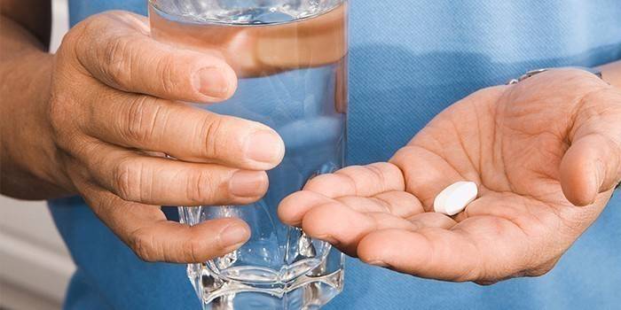 Мужчина держит в руке стакан с водой и таблетку