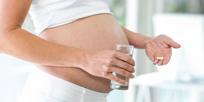 Беременная женщина с капсулами и стаканом воды в руках